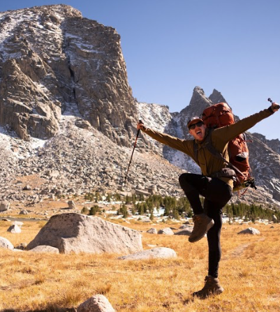 Pattie poses joyfully at the foot of a large rocky mountain