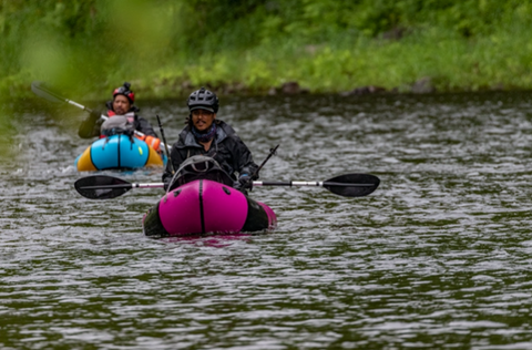 Two adventure racers paddle personal boats along a river 